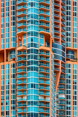 Abstract architectural detail: Full-frame view of a high-rise building facade featuring orange framing and turquoise-tinted glass windows and balconies arranged in repeating geometric patterns — South Beach.
