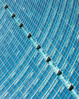 Abstract view of a modern glass skyscraper facade with repeating vertical windows and diagonal architectural details in shades of blue and cyan — Brickell, Miami.