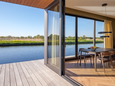 Interior of a floating home by Eiland8Architecten on the Ringvaart in Vijfhuizen, with a dining area, herringbone floor and open sliding doors leading to a wooden waterside terrace.