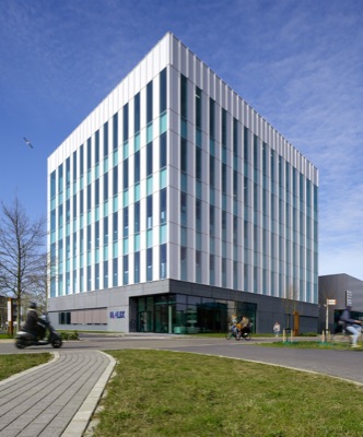 Corner view of the Halix building in Leiden with modern vertical facade elements and large windows under a clear blue sky, with cyclists on the street in front.
