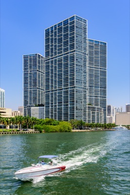 A motorboat navigates the waterway in front of the tall Icon Brickell towers, designed by Arquitectonica, under a clear blue sky.