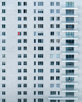 Abstract architectural detail: Pale grey residential facade with regular rows of windows and balconies and a small bright red accent among the neutral tones — Zuidas, Amsterdam.