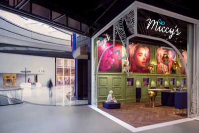 Storefront and interior of the Miccy's boutique in a shopping center, featuring decorative green walls, illuminated signage, and a herringbone floor, with a mall concourse and Zara store in the background.