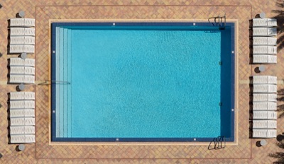 Graphic overhead photograph: Direct overhead view of a rectangular swimming pool with blue water, surrounded by a paved deck with rows of white lounge chairs and small round tables — Brickell Miami.
