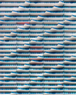 Abstract architectural detail: Full-frame architectural view of a high-rise facade with repeating horizontal rows of white balconies featuring angular, wave-like forms and tinted blue glass — Brickell, Miami.