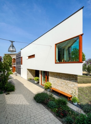 Modern residential house on Wattstraat in Nieuw Leyden, featuring an angled white upper facade with a projecting wooden window frame, a stone ground floor, and a paved pathway.