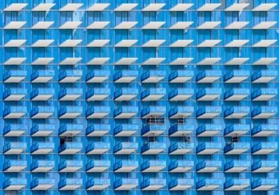 Abstract architectural detail: A repetitive pattern across a modern building facade featuring rows of white and blue balconies set against blue glass windows — Brickell, Miami.