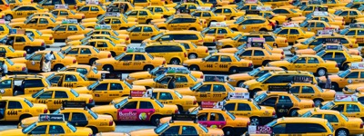Abstract urban photograph: An elevated view of a dense gathering of yellow taxis parked close together, filling the entire frame. Several car doors are open and a few individuals stand among the vehicles.